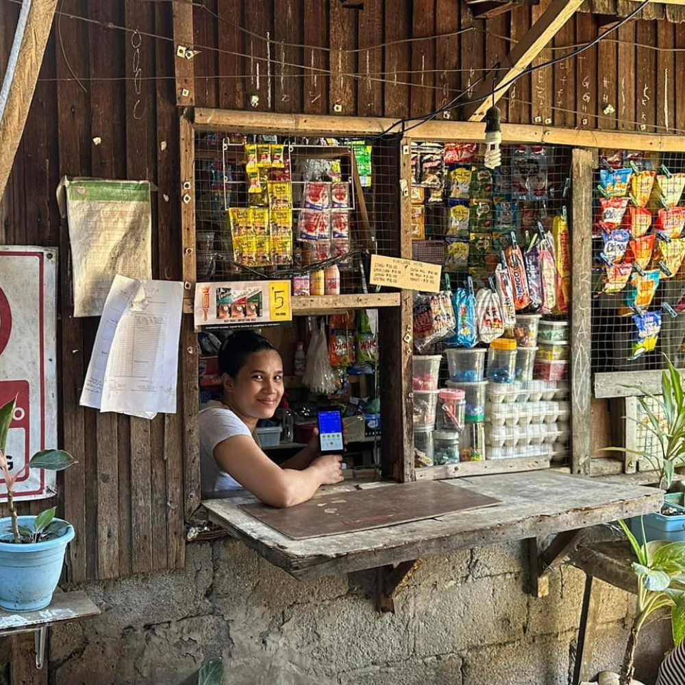 A yufin user behind the counter of her sari-sari store, holding her smartphone displaying the yufin app.