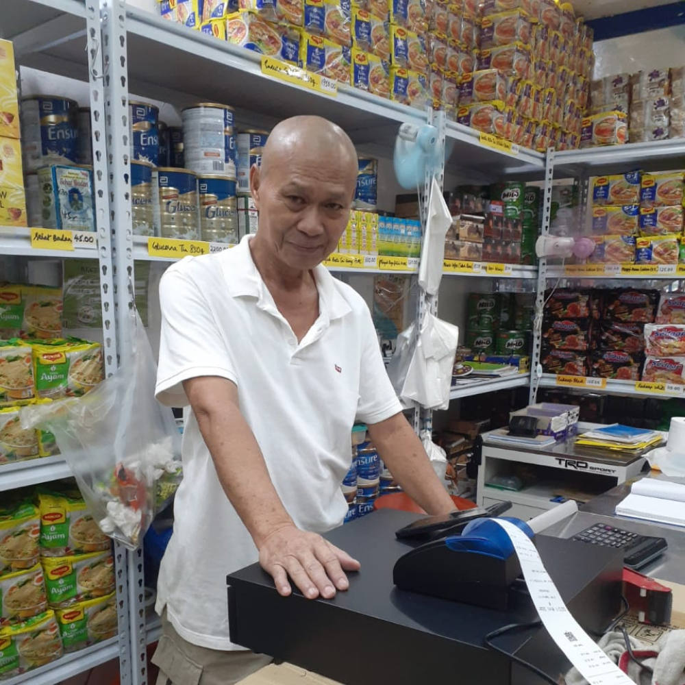 A yufin user standing behind the counter of his store, with a POS printer in front of him printing a long receipt.