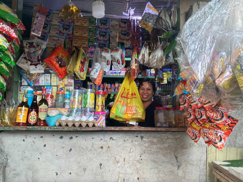 A yufin user behind the counter of her sari-sari store, holding up a plastic bag filled with her orders, fulfilled by yufin's brand partner, Lots for Less.