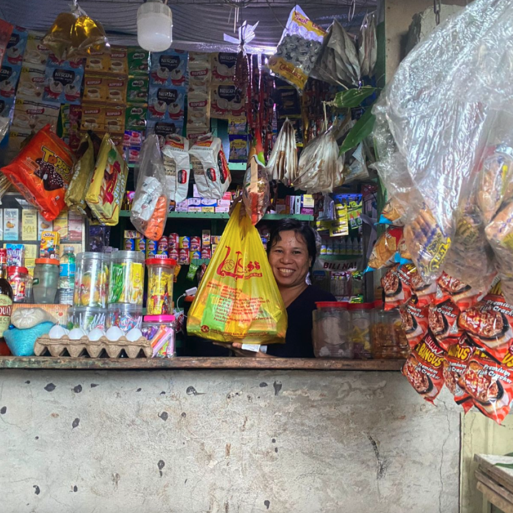 A yufin user behind the counter of her sari-sari store, holding up a plastic bag filled with her orders, fulfilled by yufin's brand partner, Lots for Less.