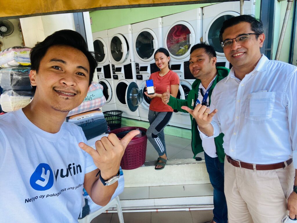 The yufin team in front of a laundromat with a yufin user, holding up her smartphone displaying the yufin app.