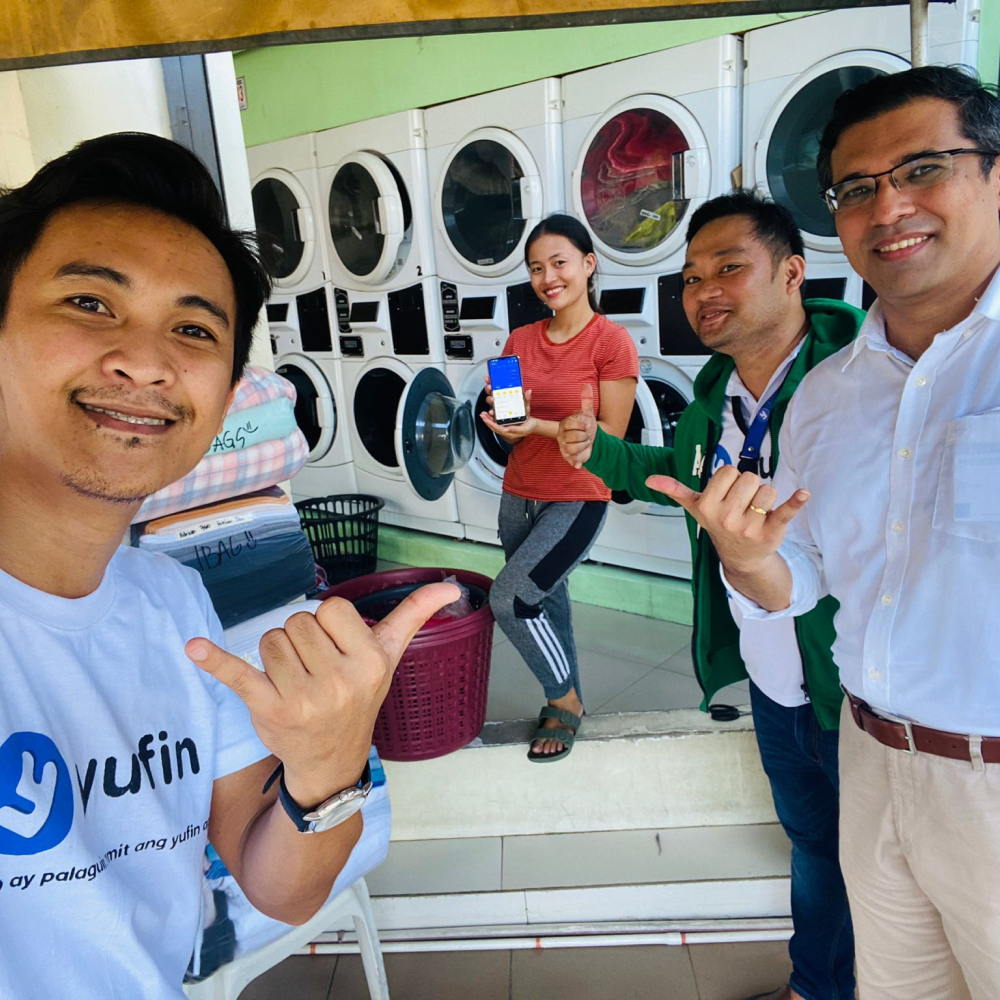 The yufin team in front of a laundromat with a yufin user, holding up her smartphone displaying the yufin app.