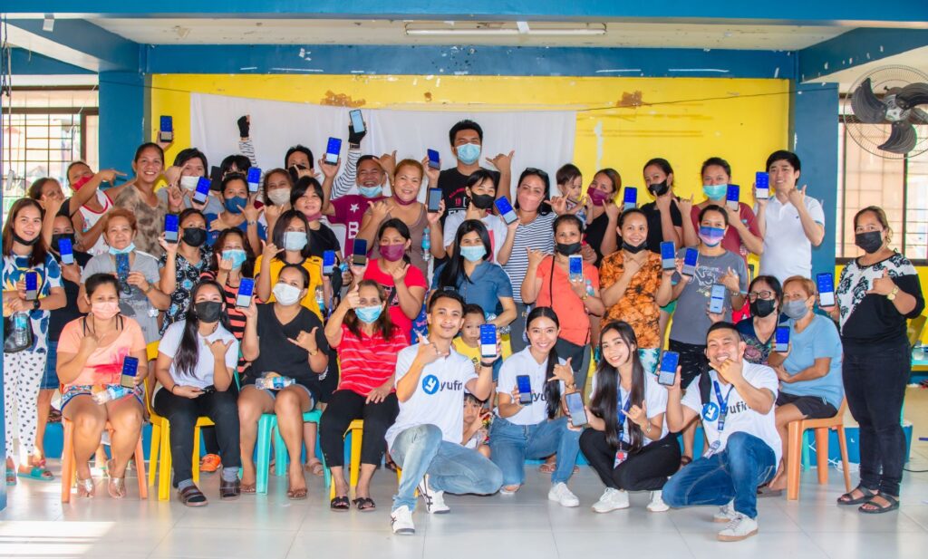 The yufin team with a group of people holding up their smartphones displaying the yufin app, while forming the yufin symbol with their hands.